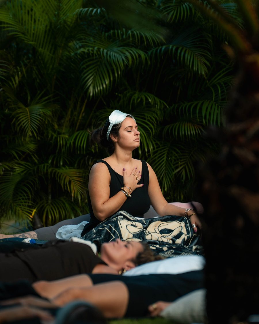 A guest sitting in stillness among palms, hand on heart